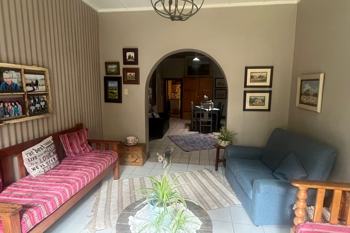 A cozy living room featuring a distinctive arched doorway leading to an adjacent dining area, finished with neutral wall tones and tiled flooring.