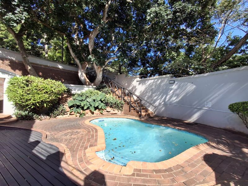 A private outdoor pool area featuring brick paving, a retaining wall, and a metal staircase leading to an elevated garden section.