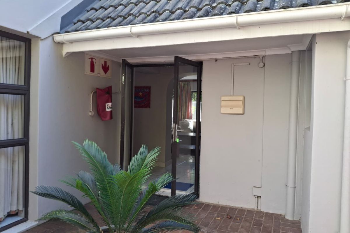 A view of the rear entrance featuring brick paving, a tiled roof overhang, and mounted fire safety equipment.