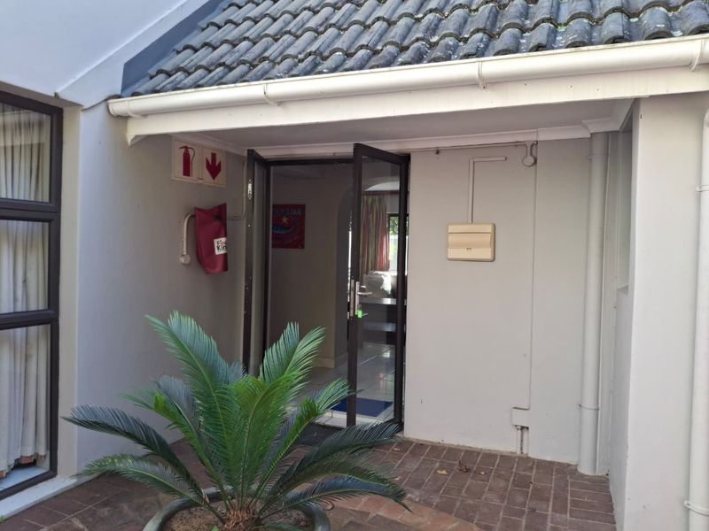 A view of the rear entrance featuring brick paving, a tiled roof overhang, and mounted fire safety equipment.