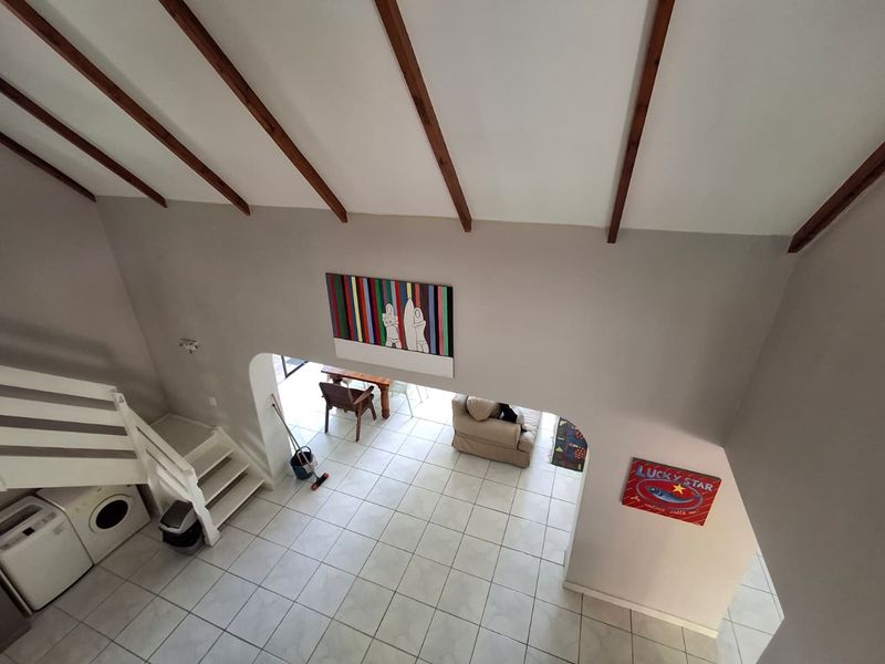 An elevated view of an open-plan living area featuring exposed timber ceiling beams, tiled flooring, and a staircase with a white balustrade.