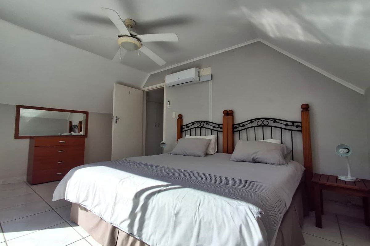 A bedroom featuring a sloped ceiling, tiled flooring, a ceiling fan, and a wall-mounted air conditioning unit.