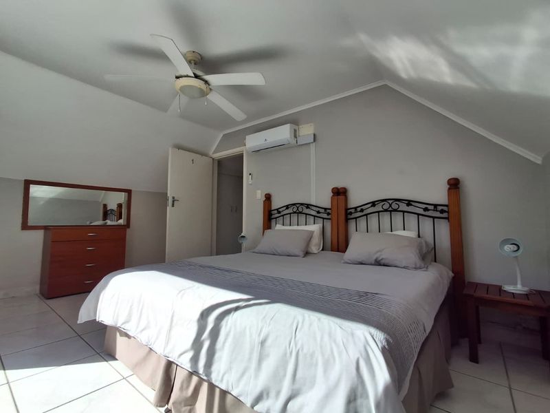 A bedroom featuring a sloped ceiling, tiled flooring, a ceiling fan, and a wall-mounted air conditioning unit.