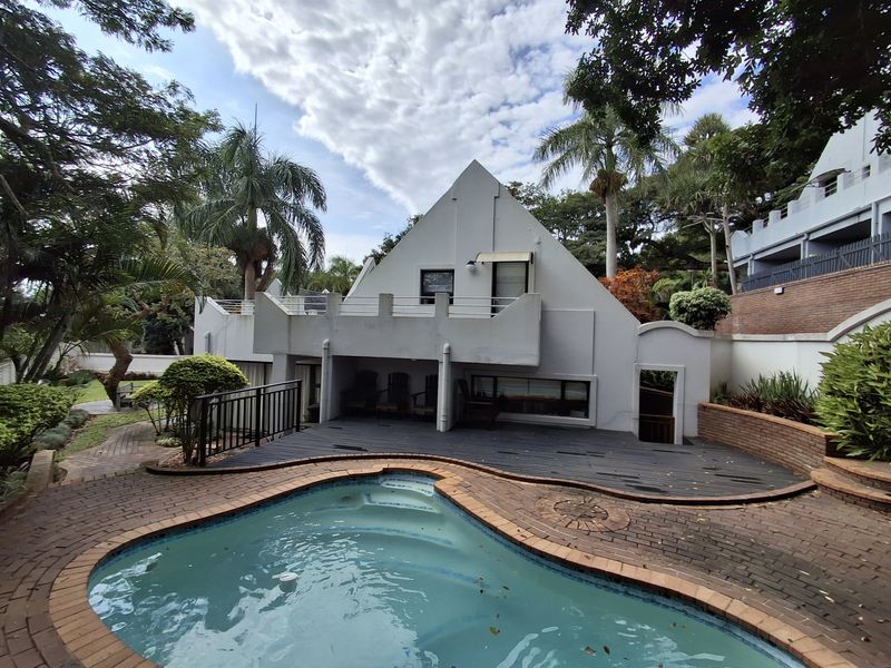 Rear exterior view featuring a swimming pool, brick paved surround, timber deck, and a multi-level dwelling with a balcony.