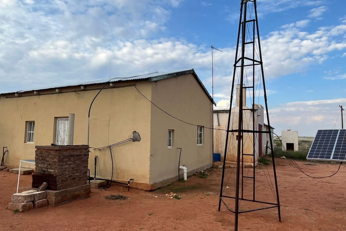 Rear view of a farm building featuring a traditional windmill, solar panel installation, and an external brick fireplace structure.