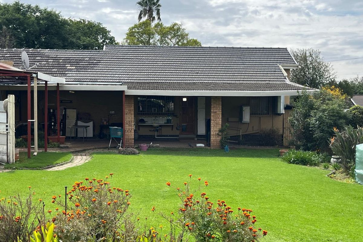 Rear view of the house featuring a covered patio area, brick pillars, and a well-maintained lawn with established garden beds.
