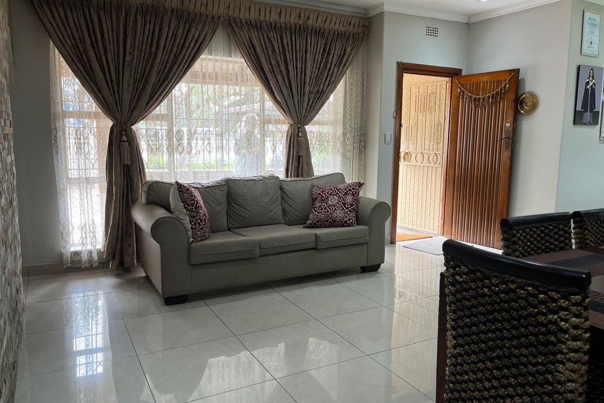 A bright living room featuring polished porcelain floor tiles, recessed downlighting, and a timber entrance door with an integrated security gate.