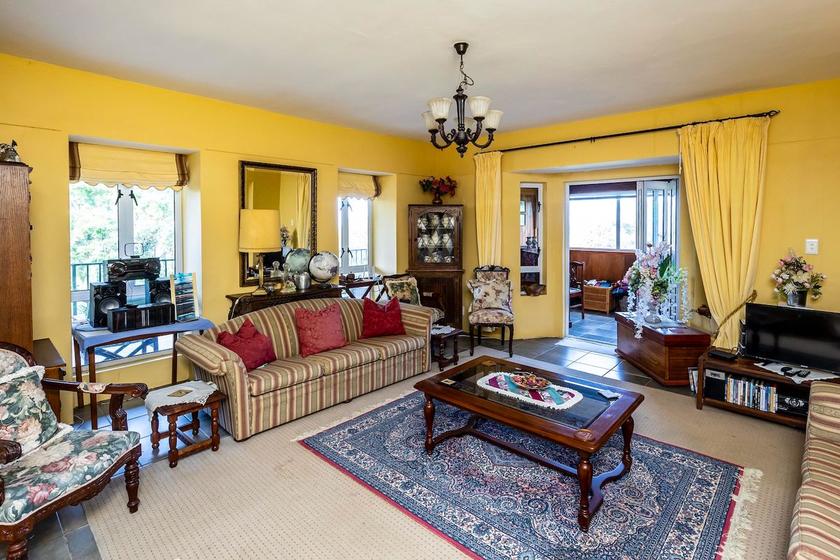 Spacious living room featuring yellow walls, a central chandelier, and bi-fold doors leading to an adjacent sunroom or patio area.