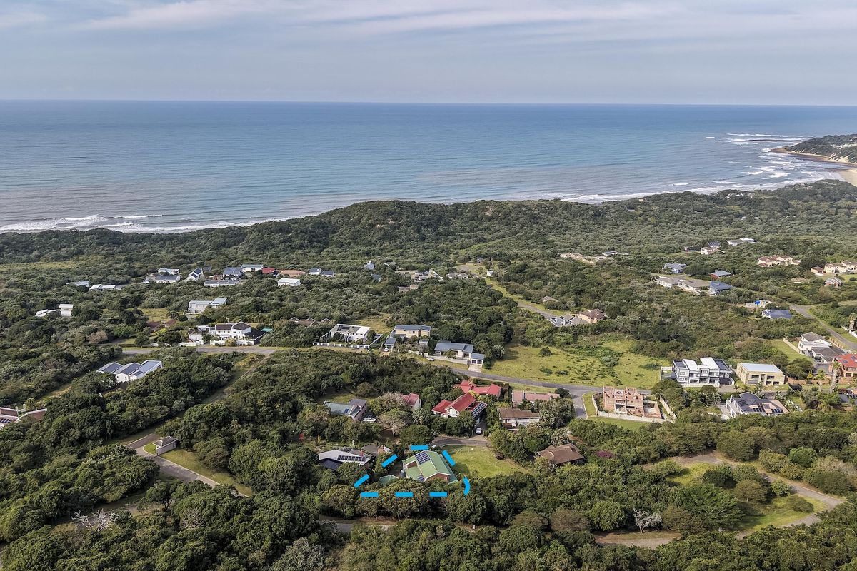 Aerial view of a coastal residential property nestled within a lush, green landscape, featuring solar panels on the roof and proximity to the ocean.