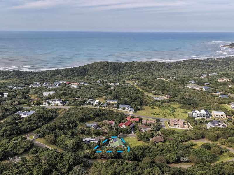 Aerial view of a coastal residential property nestled within a lush, green landscape, featuring solar panels on the roof and proximity to the ocean.