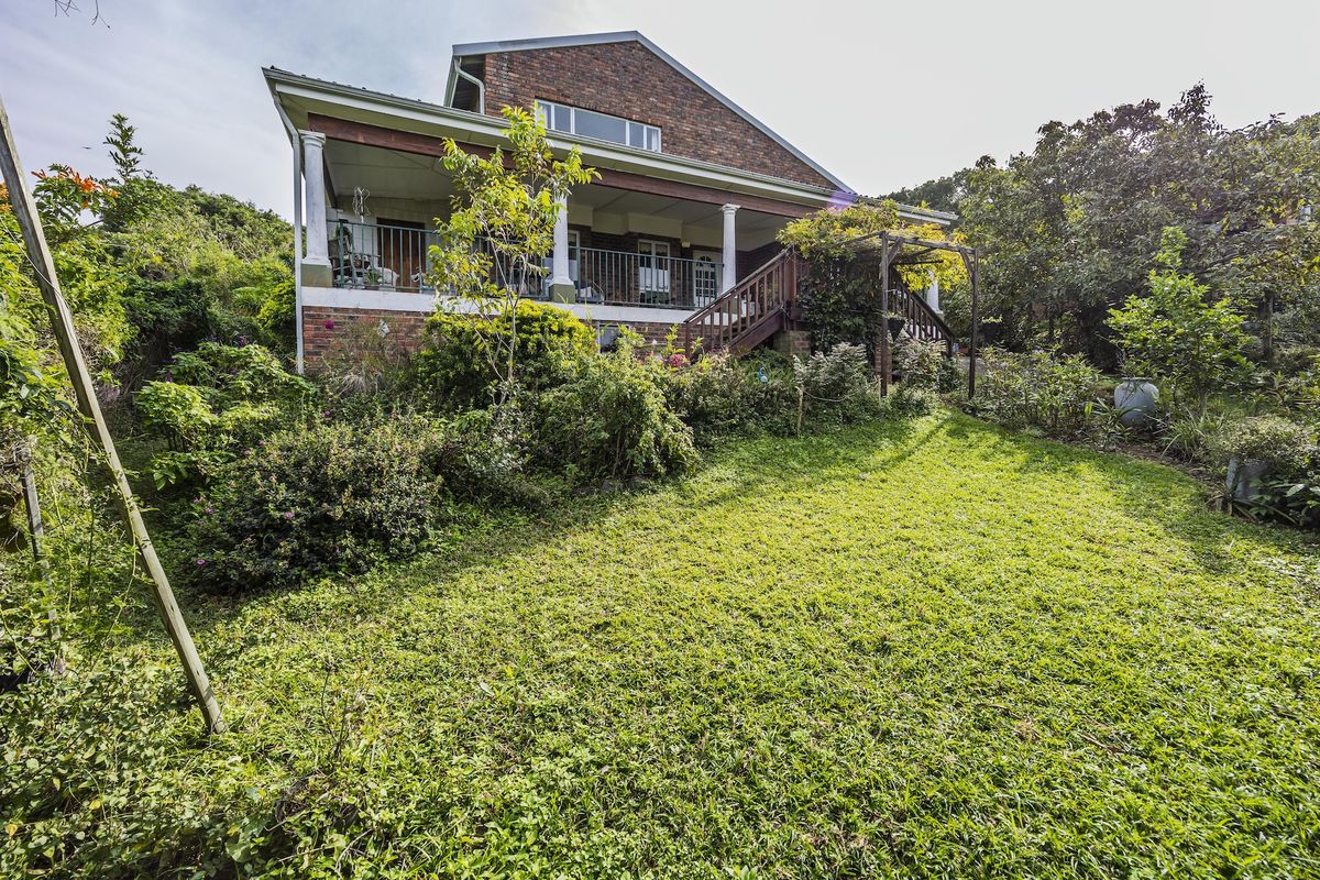 Rear view of a brick house featuring a covered patio, wooden staircase, and a landscaped garden area.