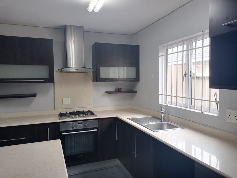 A functional kitchen featuring dark cabinetry, stone countertops, a gas hob, built-in oven, and stainless steel extractor fan with security bars on the window.