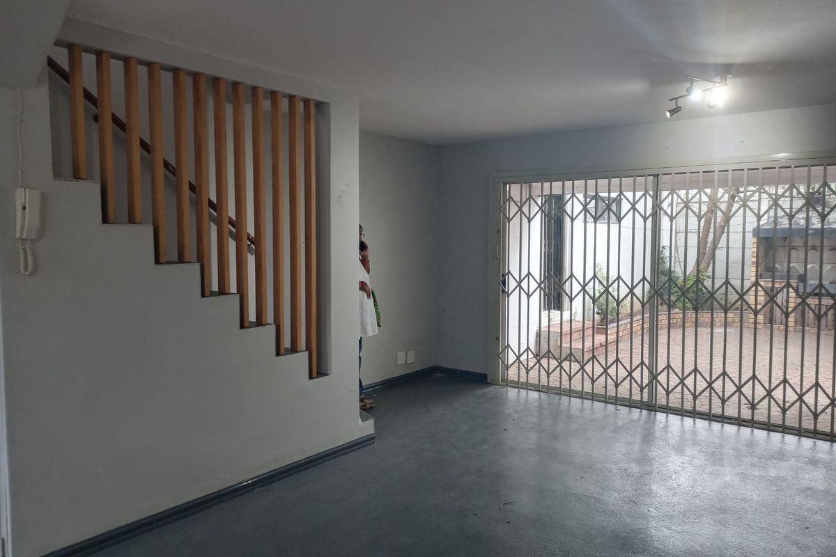 An open-plan living area featuring a wooden staircase balustrade, sliding glass doors with security gates, and direct access to an outdoor patio area.