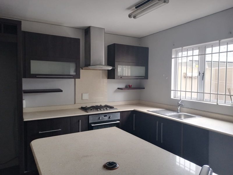 A functional kitchen featuring dark wood cabinetry, stone countertops, a built-in gas hob, oven, and a central island with a stainless steel sink.