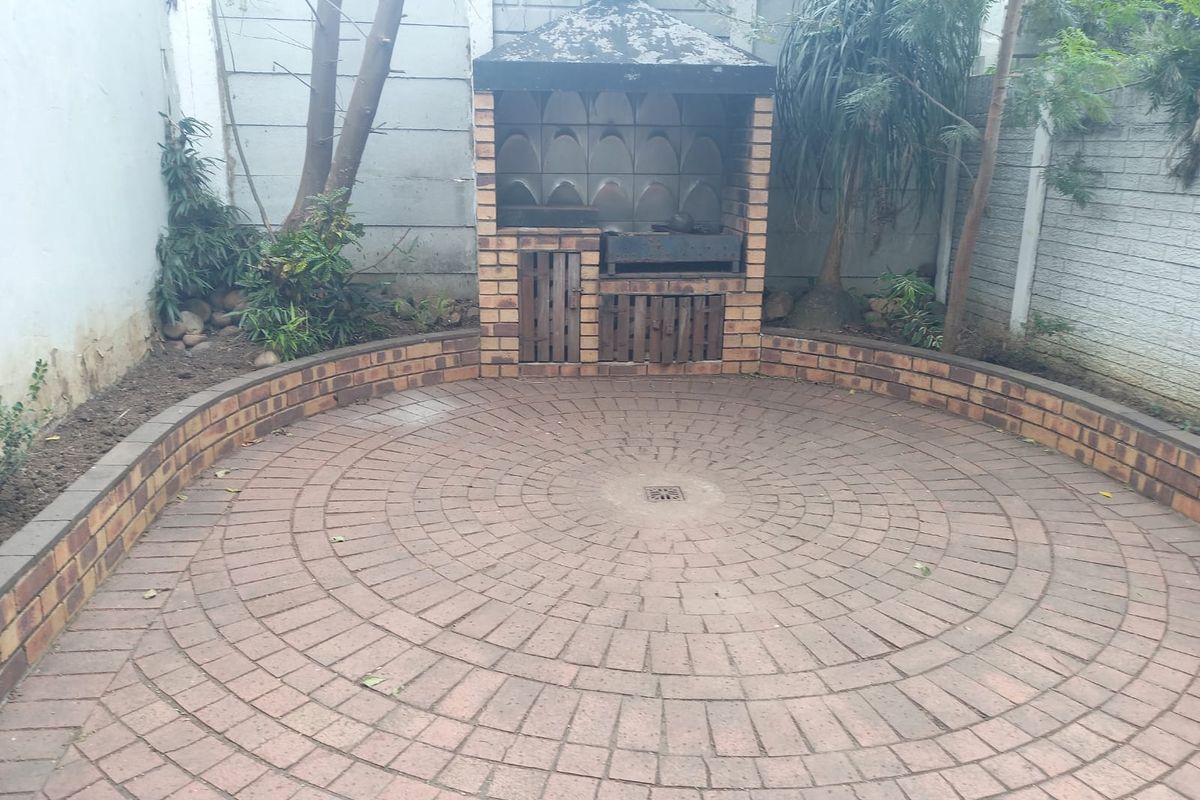 Rear courtyard featuring a circular brick paved patio and a built-in brick braai area, enclosed by perimeter walls.