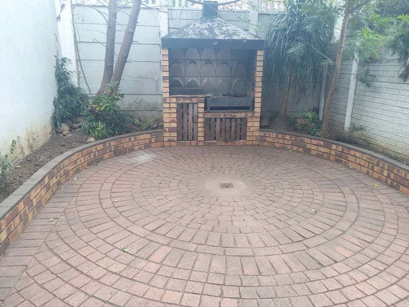 Rear courtyard featuring a circular brick paved patio and a built-in brick braai area, enclosed by perimeter walls.