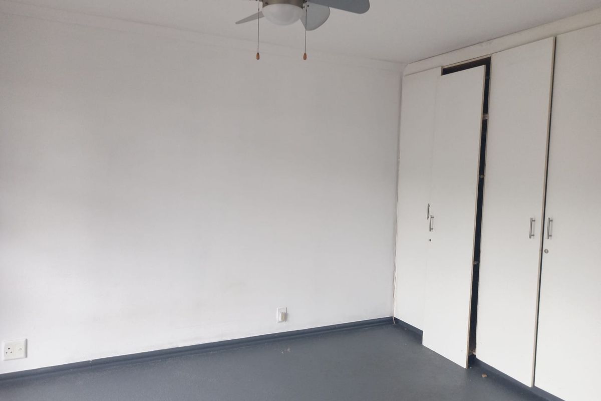 An empty bedroom featuring a ceiling fan and built-in cupboards with a dark floor finish.