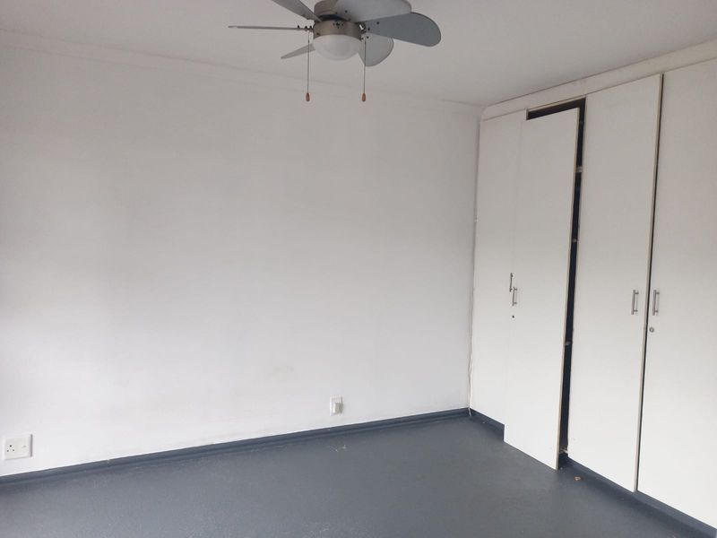 An empty bedroom featuring a ceiling fan and built-in cupboards with a dark floor finish.