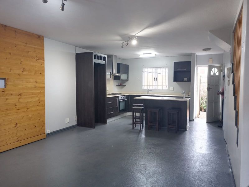 Open-plan living area featuring a modern kitchen with built-in cabinetry, island, and wood-paneled feature wall, leading to an exterior entrance.