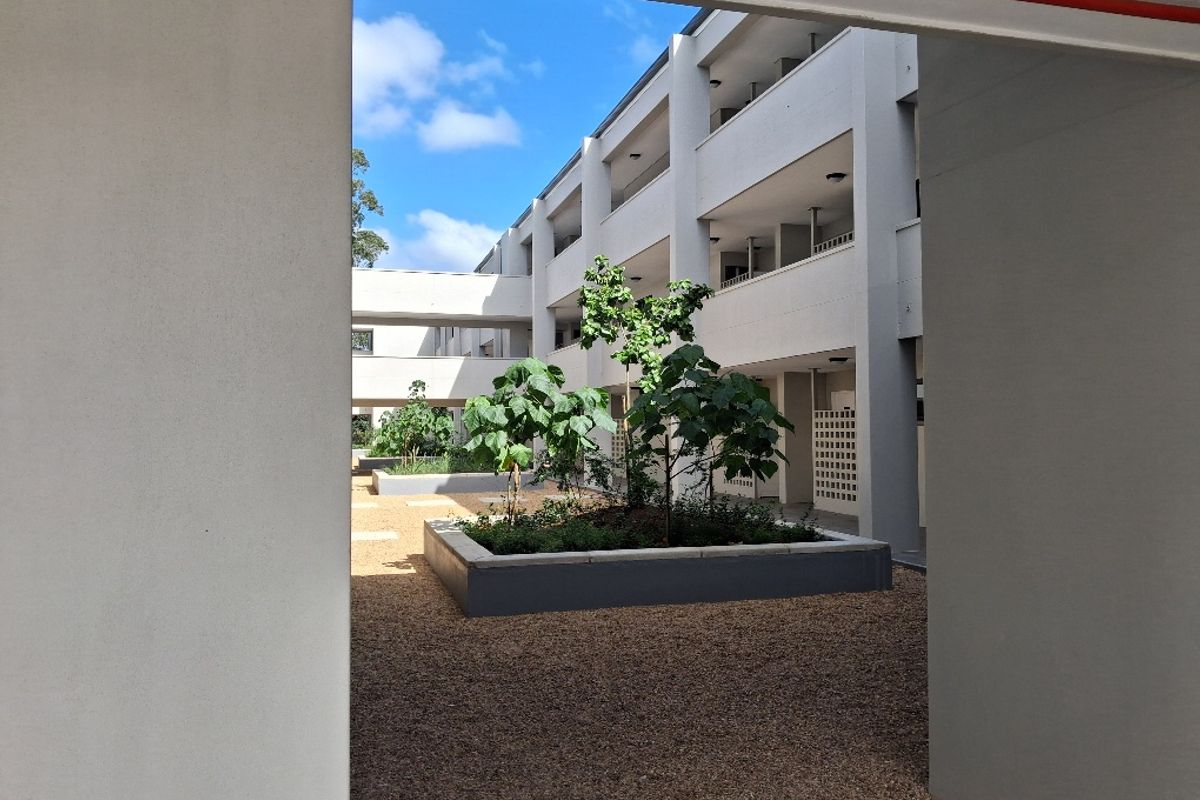 A view of the apartment complex courtyard featuring raised garden beds, gravel landscaping, and multi-level walkways.