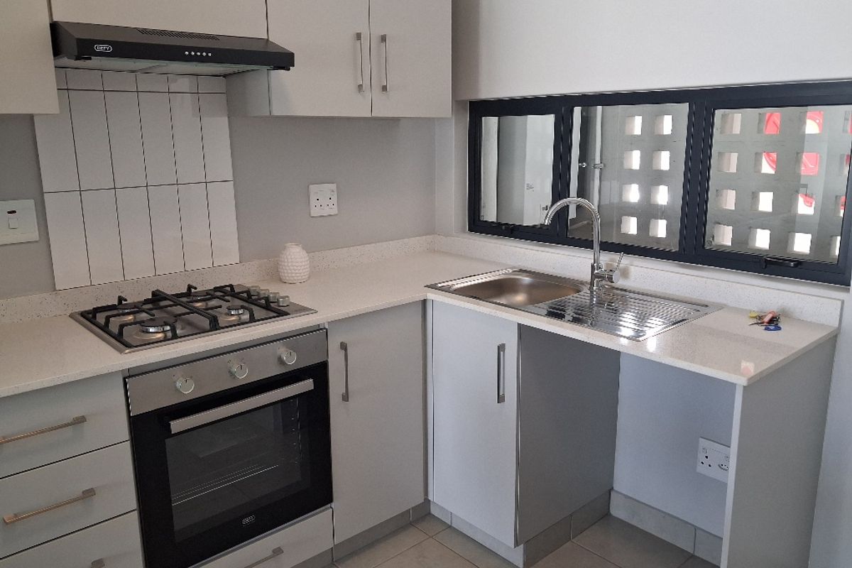 Modern kitchen featuring light grey cabinetry, quartz countertops, a gas hob, built-in oven, extractor fan, and a stainless steel sink.