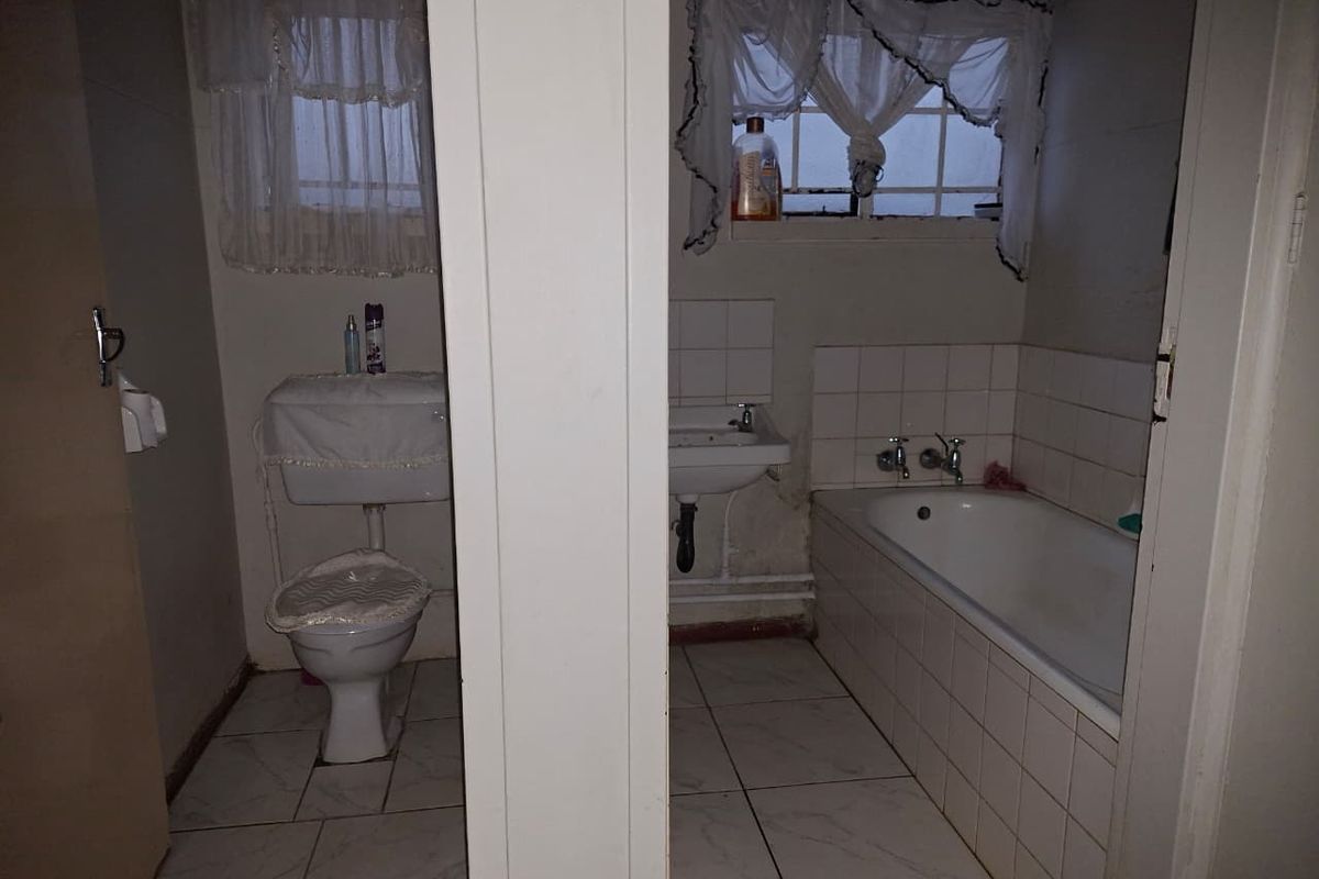 A dated bathroom featuring a standard bathtub, wall-mounted basin, and toilet, requiring cosmetic updates to modernize the space.