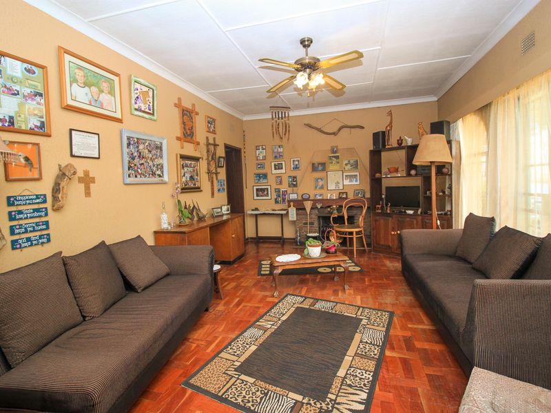 A living room featuring traditional parquet flooring, a central ceiling fan, and a built-in fireplace with integrated shelving.