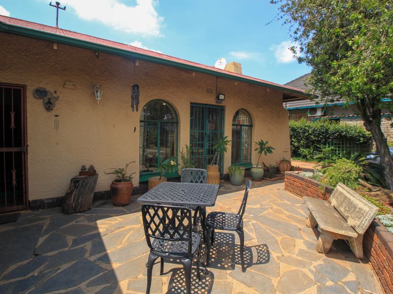 A paved outdoor patio area featuring arched windows, a built-in stone bench, and a brick planter box, providing a functional space for outdoor relaxation.