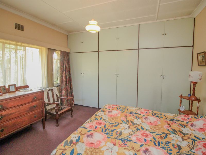 A bedroom featuring extensive built-in cupboards, carpeted flooring, and security bars on the windows. The space offers a functional layout with dated finishes.