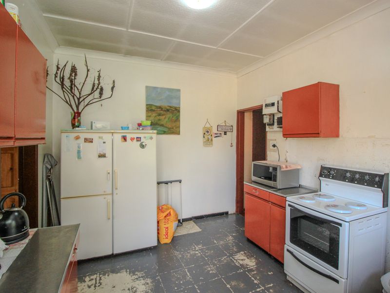 A dated kitchen featuring original cabinetry, a freestanding stove, and worn flooring, offering significant potential for a modern renovation and cosmetic update.