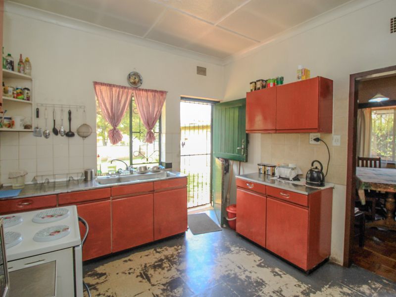 A functional kitchen featuring original cabinetry, stainless steel sink, and tiled splashbacks, requiring cosmetic updates to modernize the space.