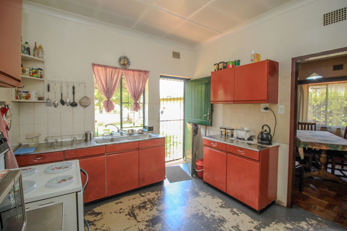 A functional kitchen featuring dated cabinetry, a stainless steel sink, and a tiled splashback, with direct access to the exterior via a security gate.