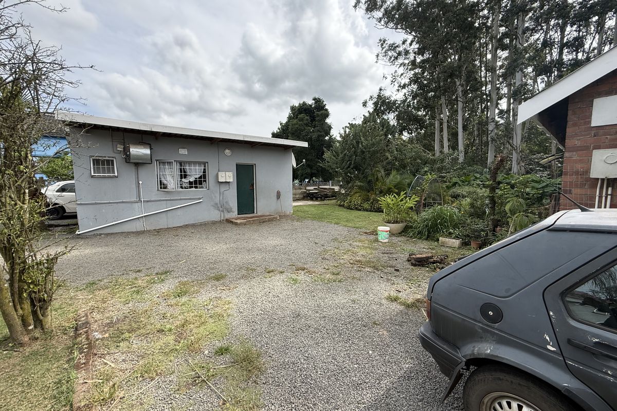 Rear exterior view of the property featuring a gravel driveway, external geyser, and established garden area.