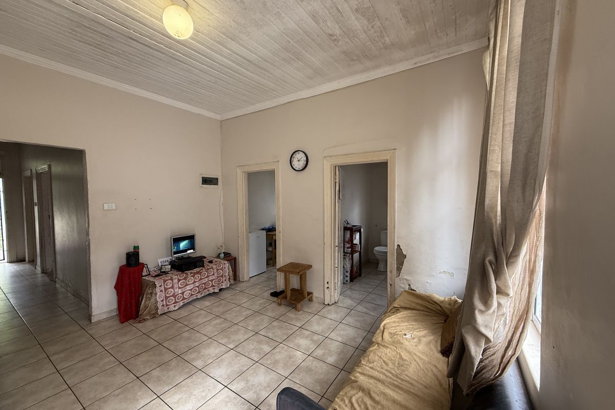 Living room featuring tiled flooring and a timber ceiling, showing signs of wear and requiring cosmetic repairs to the wall finishes.
