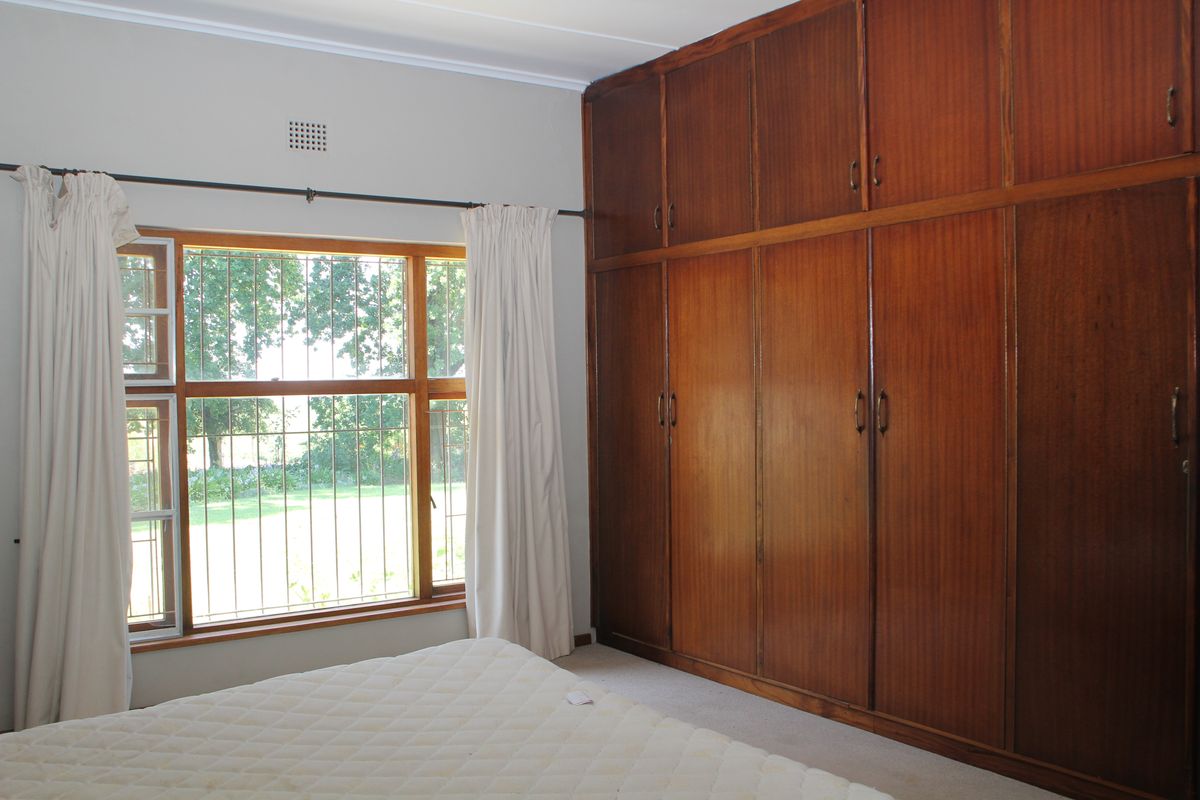 Bedroom featuring extensive floor-to-ceiling built-in wooden cabinetry and a large window with security bars overlooking the garden.