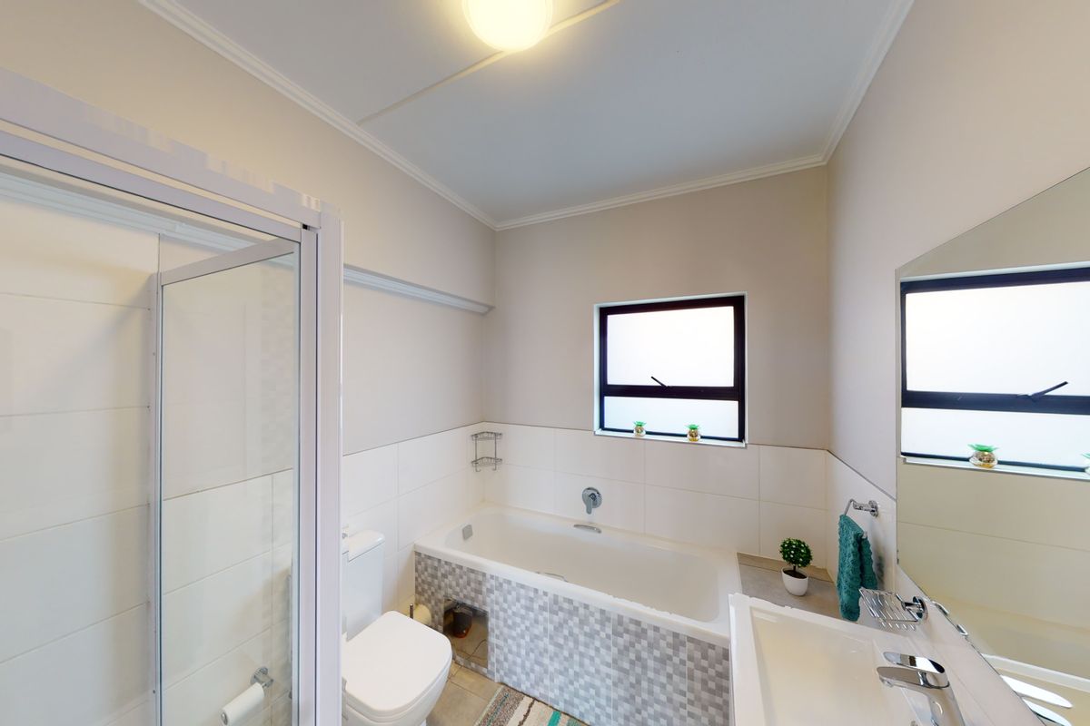A clean, functional bathroom featuring a built-in bathtub with mosaic tiling, a separate glass-enclosed shower, and a wall-mounted vanity mirror.