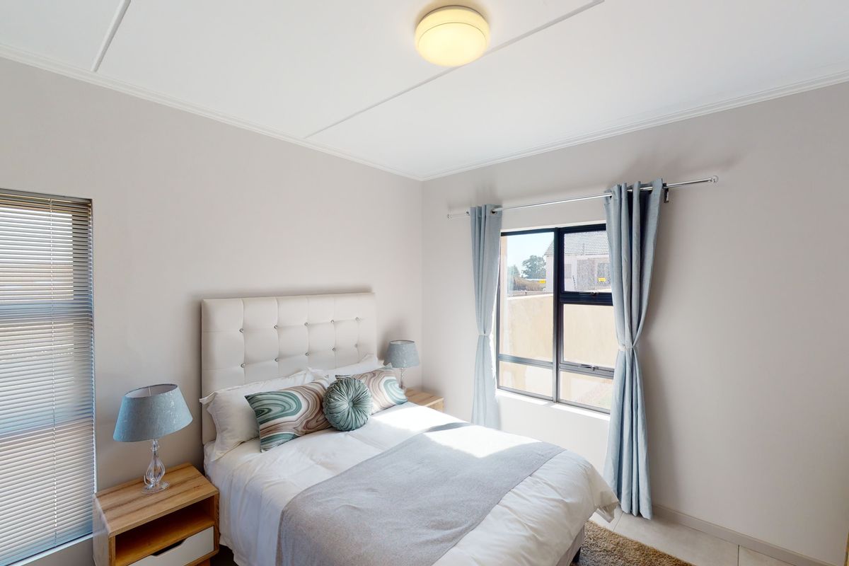 A bright bedroom featuring neutral walls, tiled flooring, and large windows with fitted blinds and curtains, providing natural light.