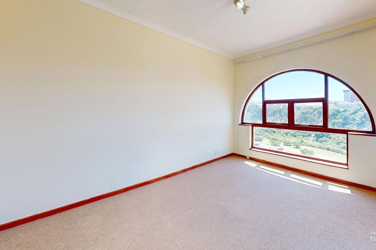 A bright, empty bedroom featuring a distinctive arched window with scenic views and neutral carpet flooring.