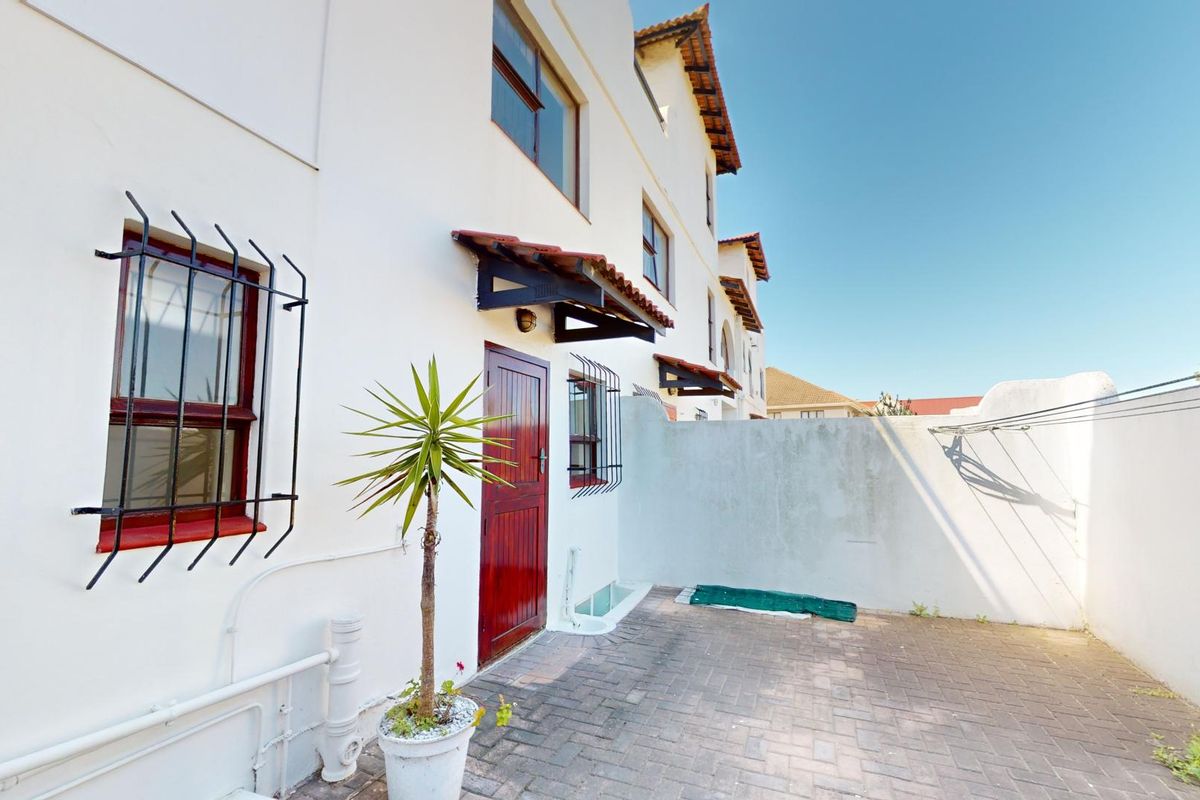 A private rear courtyard featuring paved flooring, security bars on windows, and a small tiled awning over the entrance door.