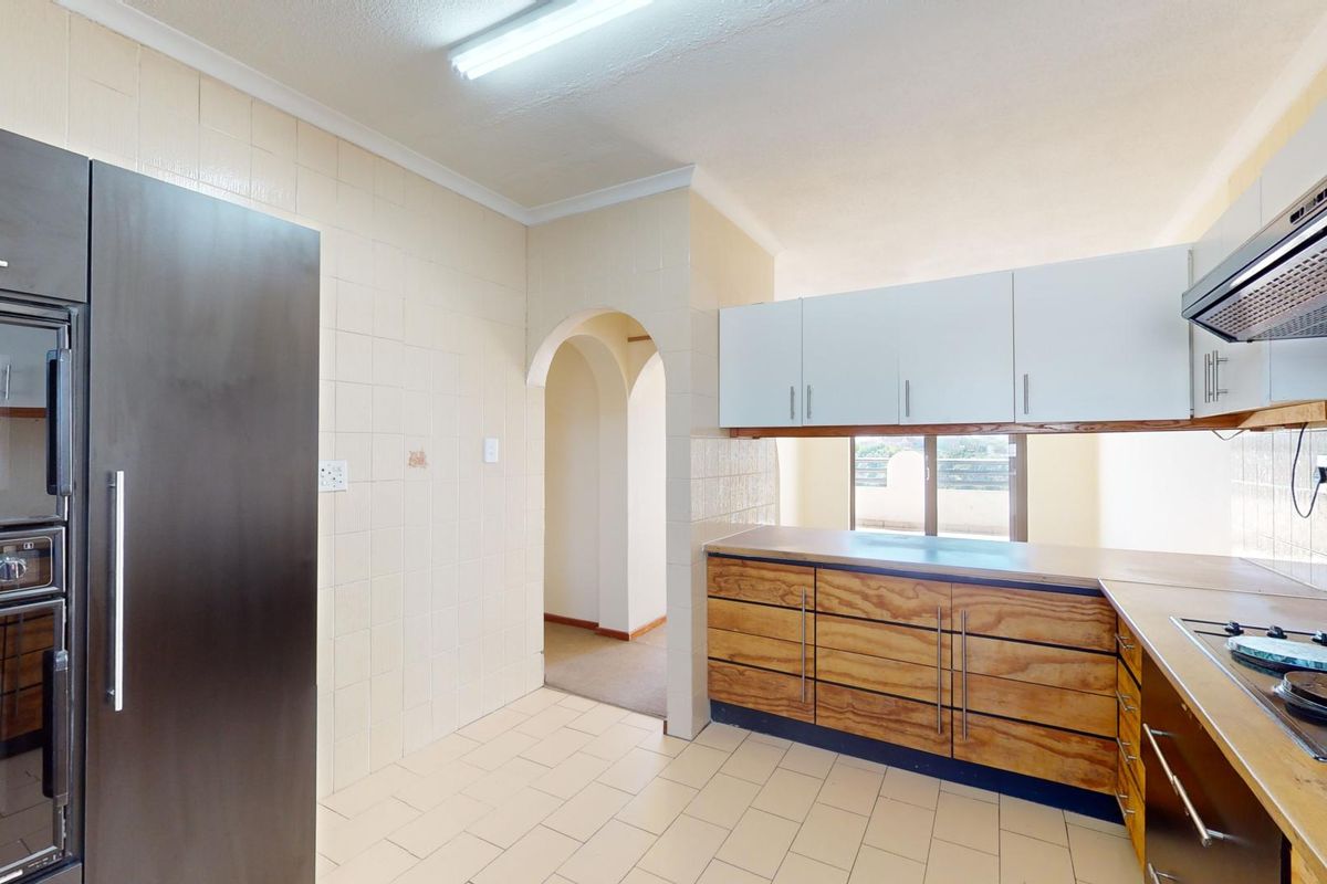 A functional kitchen featuring built-in cabinetry, a hob, an extractor fan, and a built-in oven, with tiled flooring and a classic arched entryway.