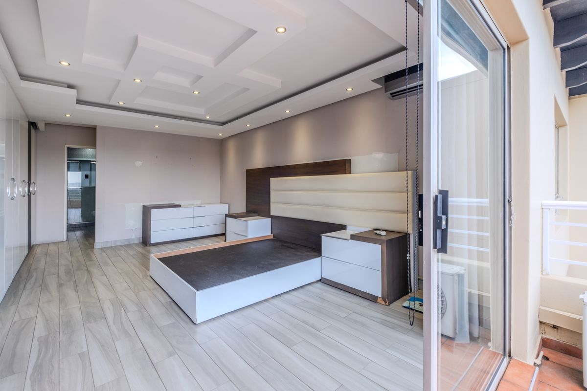 Spacious bedroom featuring a modern recessed ceiling with downlights, built-in headboard, integrated cupboards, and direct access to a private balcony through sliding glass doors.