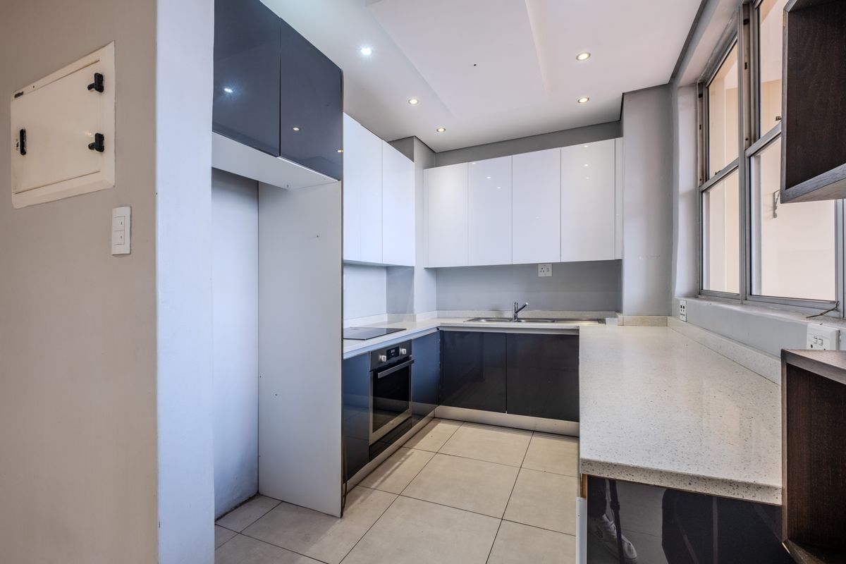 Modern kitchen featuring sleek two-tone cabinetry, stone countertops, integrated oven and hob, and tiled flooring in a clean, contemporary layout.