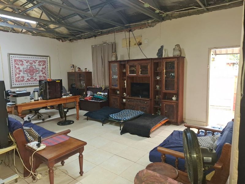 Spacious living area featuring ceramic floor tiles and exposed steel roof trusses, requiring ceiling installation and general wall repairs to improve finish.