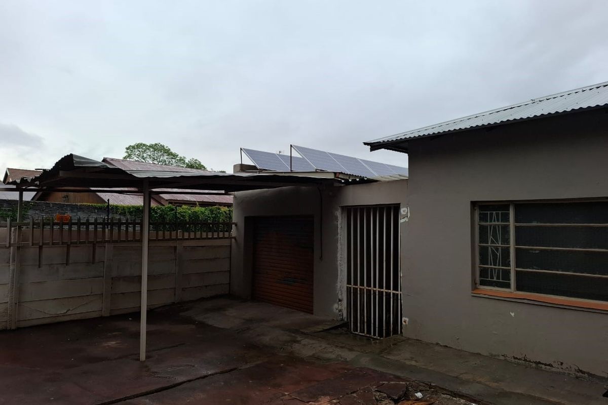 Rear exterior view showing a carport, garage access, security gate, and roof-mounted solar panels on a residential property.