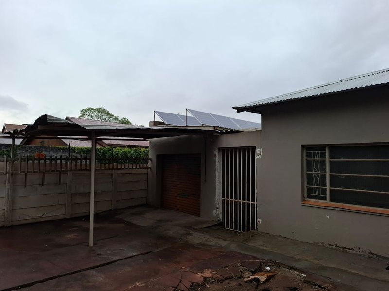 Rear exterior view showing a carport, garage access, security gate, and roof-mounted solar panels on a residential property.