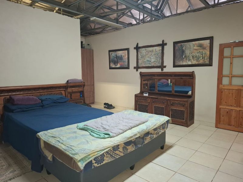 Spacious bedroom featuring tiled flooring and exposed steel roof trusses, offering a unique industrial aesthetic with potential for ceiling installation.