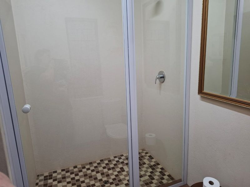 A functional bathroom featuring a glass-enclosed shower with a tiled floor and a wall-mounted mirror.