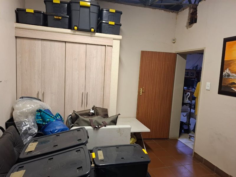 A utility space featuring built-in cupboards and tiled flooring, currently used for storage with visible wall and ceiling damage requiring repair.