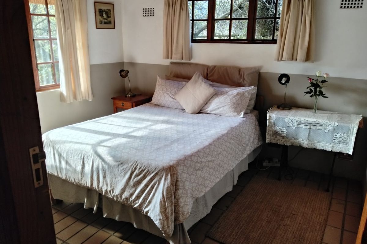 A cozy bedroom featuring rustic terracotta floor tiles, timber-framed windows, and a neutral two-tone wall finish, offering a warm and traditional farm-style aesthetic.