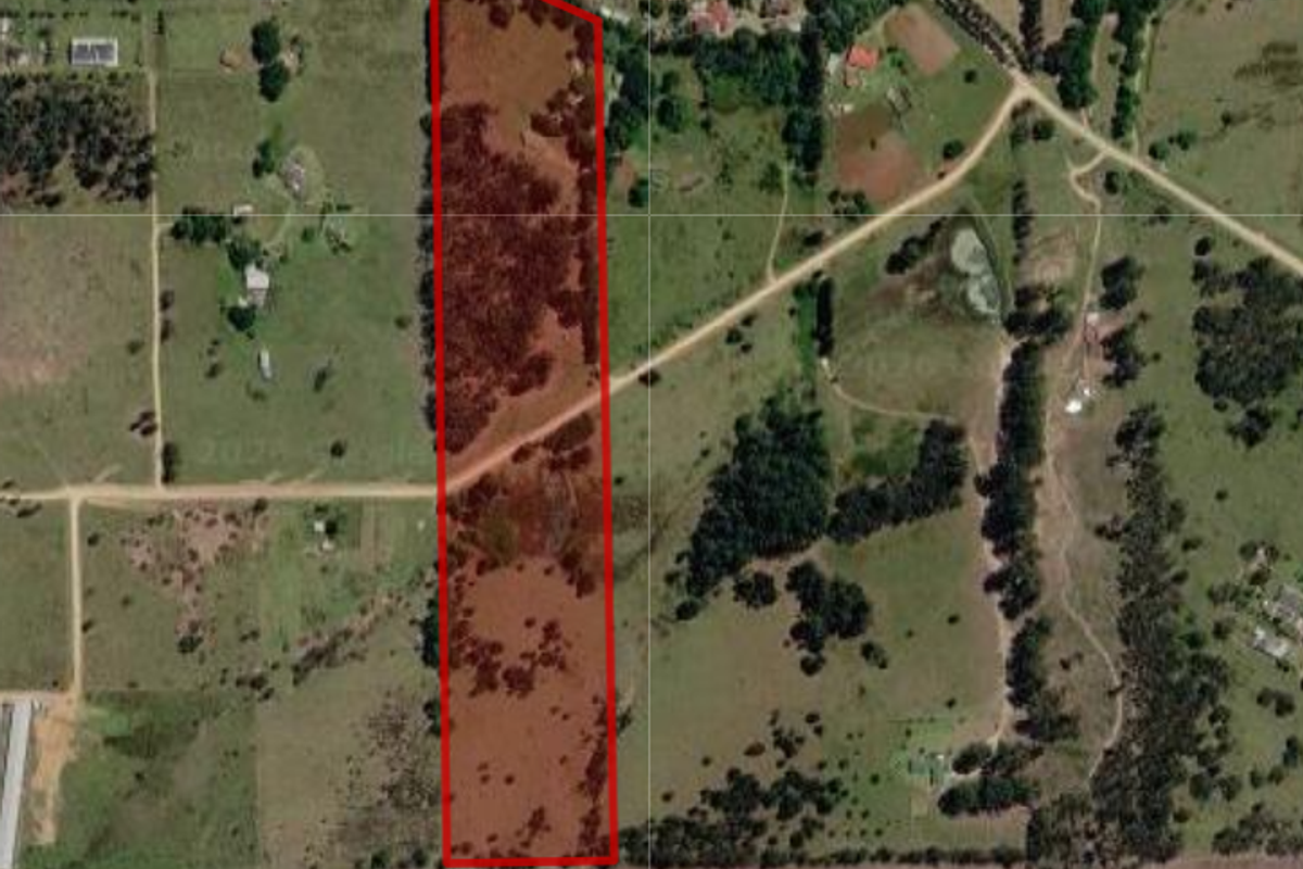 An aerial view of a large, rectangular farm property plot outlined in red, showcasing the surrounding rural landscape and access roads.